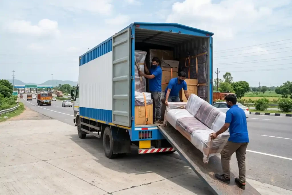Movers loading a wrapped sofa into a truck for interstate household shifting on a highway