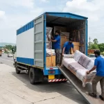 Movers loading a wrapped sofa into a truck for interstate household shifting on a highway